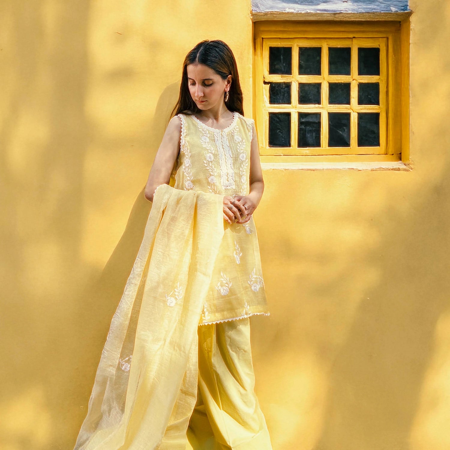 Young girl in a yellow traditional outfit standing against a yellow wall with a window.